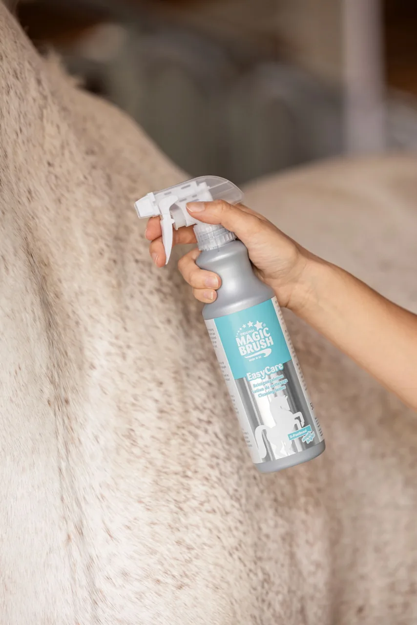 Hand sprüht türkisfarbenes Trockenpflege-Spray der Magic-Brush-Pflegeserie auf helles Pferdefell