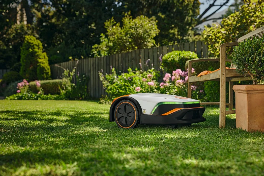 STIHL iMOW 7 Mähroboter im gepflegten Gartenrasen neben Sitzbank und Beeten