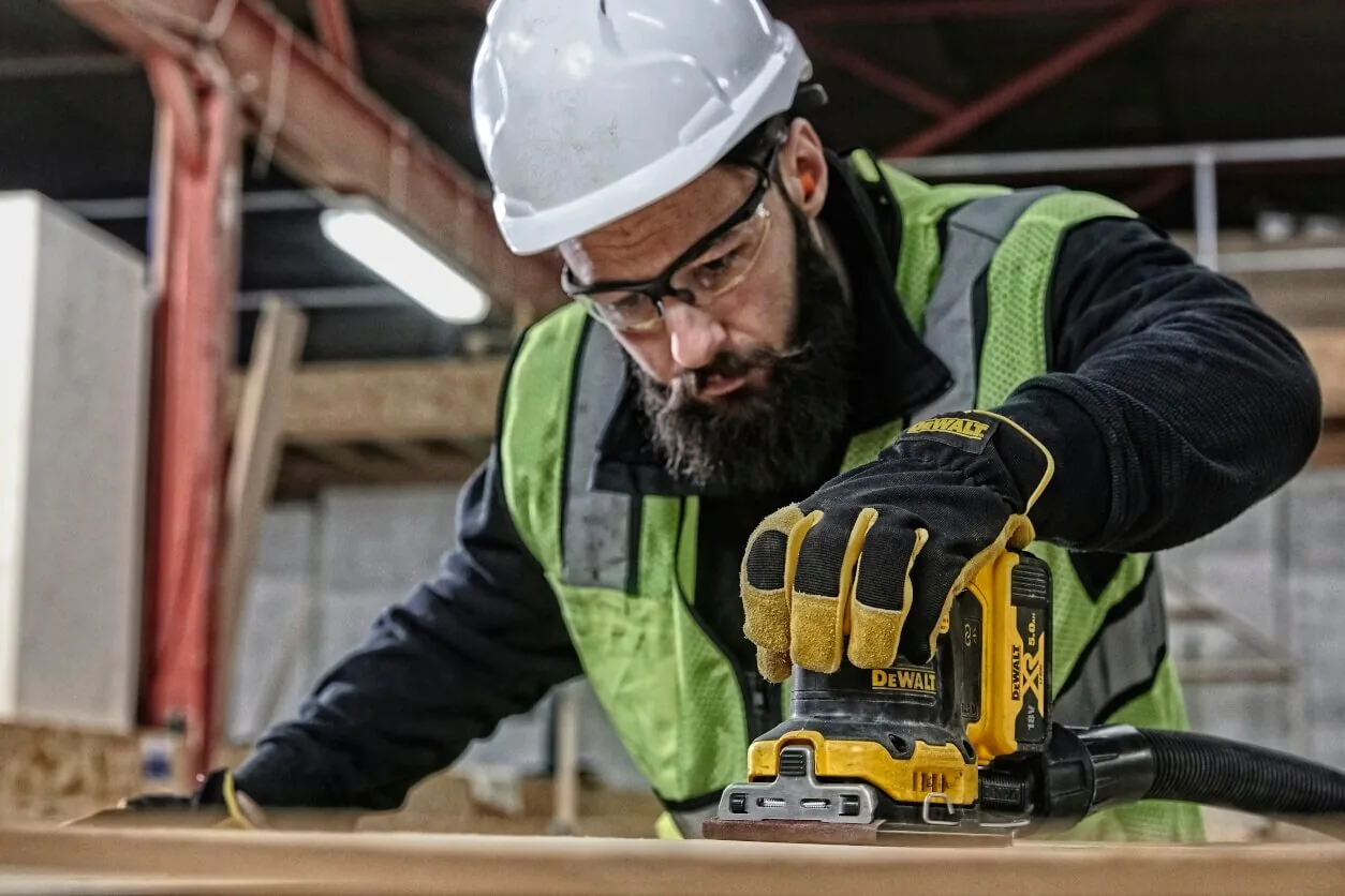 Mann schleift mit dem DeWalt DCW200NT Akku-Schwingschleifer ein Brett (Helm)