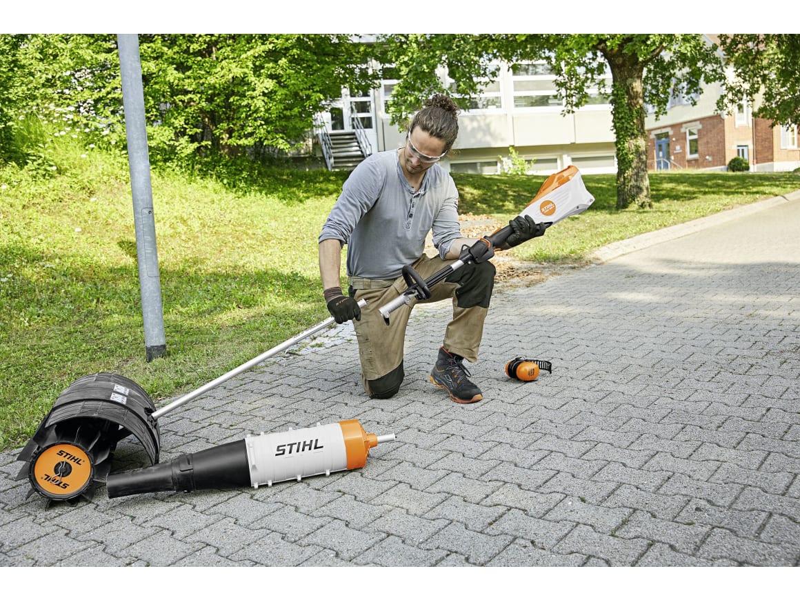 Frau legt den STIHL KMA 135 R Akku-KombiMotor mit Mähkopf-Aufsatz auf dem Weg ab