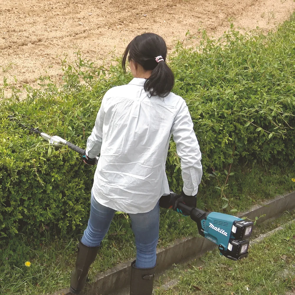 Frau bearbeitet mit dem Makita DUX60Z Multifunktionsantrieb und zwei Akkus eine Hecke