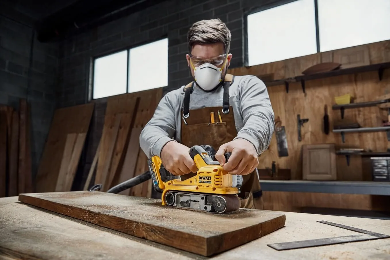 Mann schleift mit dem DeWalt DCW220NT Akku-Bandschleifer in der Werkstatt (Maske)