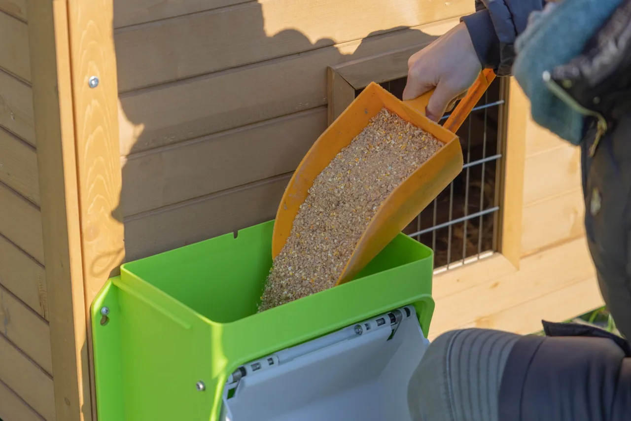 Person füllt mit einer gelben Schaufel Futter in den Kerbl SmartCoop Automaten