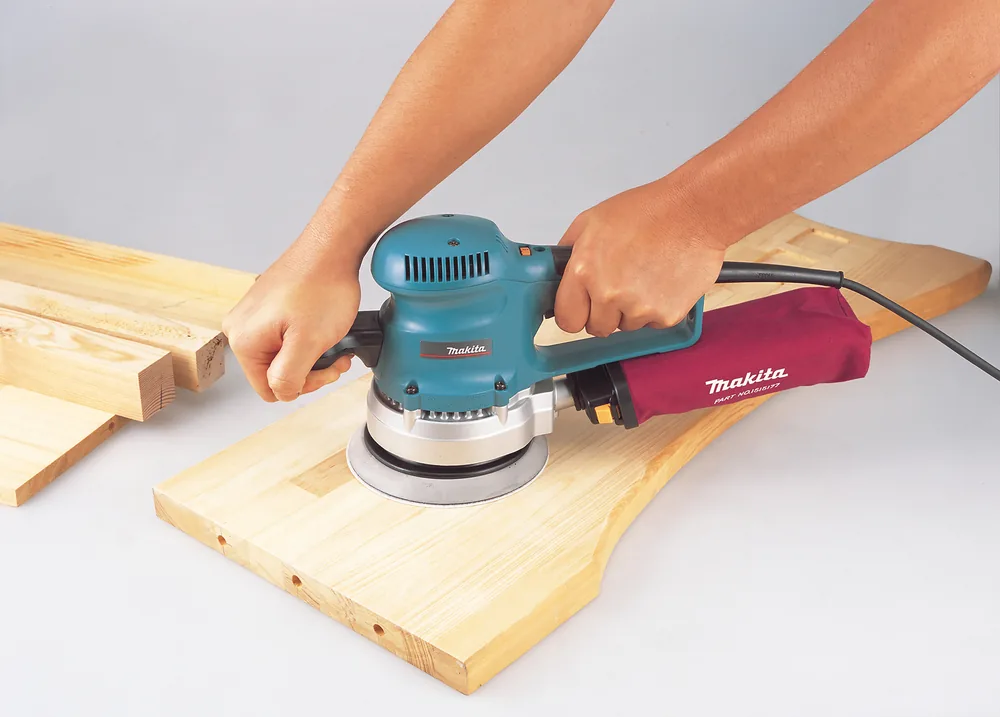 Makita BO6030JX Exzenterschleifer im Einsatz beim Schleifen eines Holzbretts