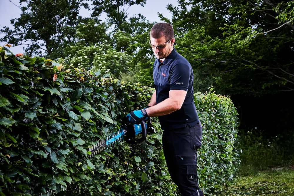 Anwender schneidet mit der Makita DUH601Z Akku-Heckenschere eine hohe Hecke