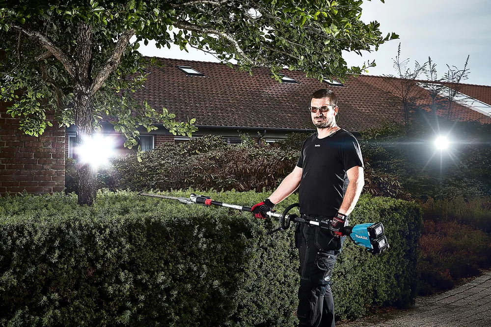 Mann schneidet mit dem Makita DUX60Z und langem Heckenschneider-Aufsatz eine Hecke