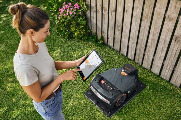 Frau bedient den STIHL iMOW 7 EVO Mähroboter per Tablet im Garten