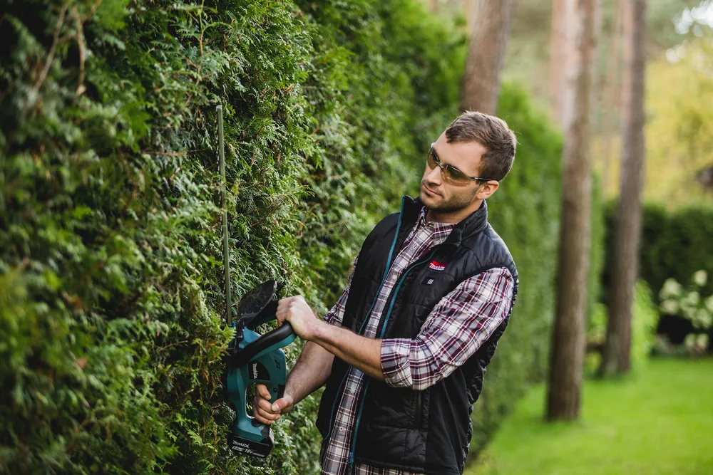 Mann mit der Makita DUH523Z Akku-Heckenschere vor einer Hecke
