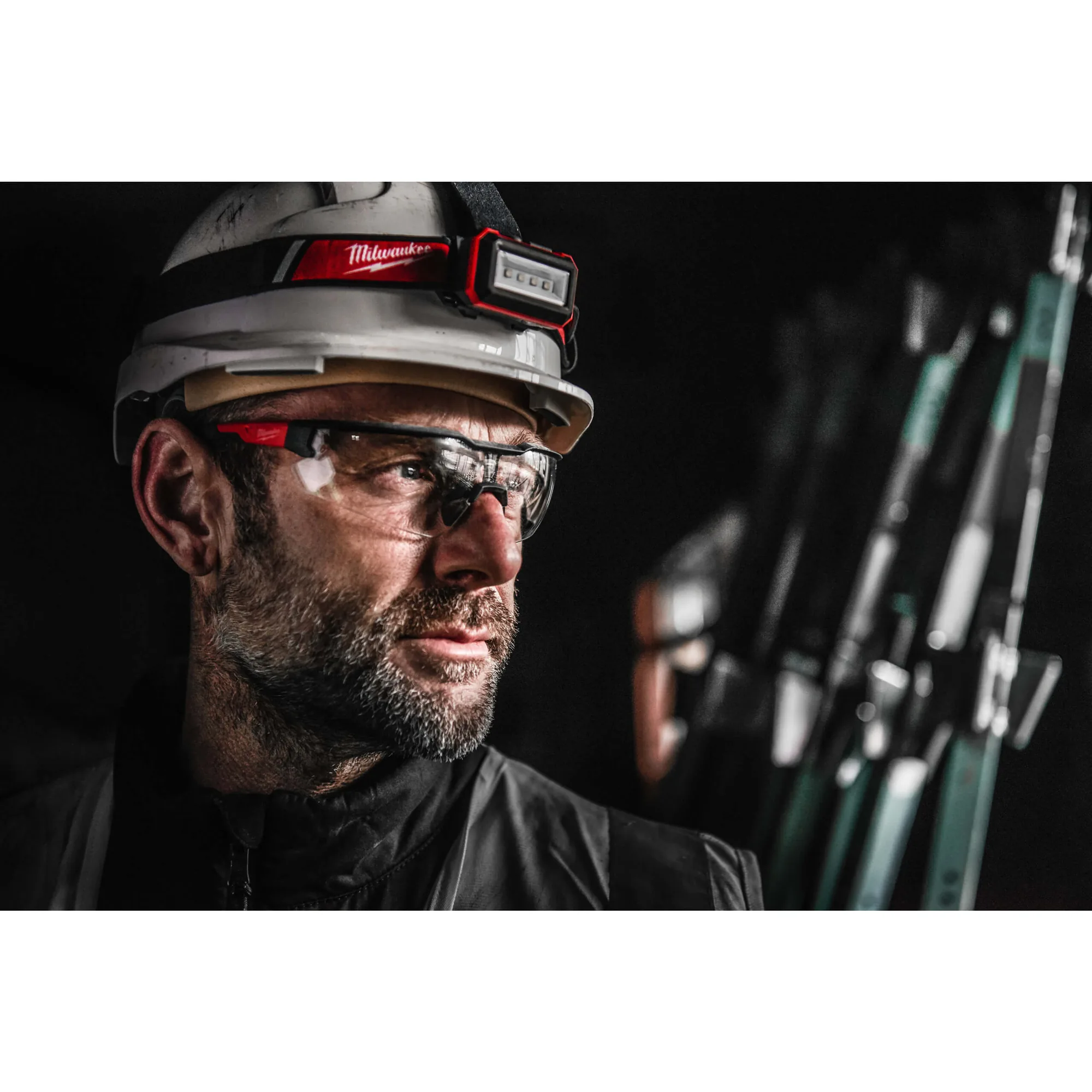 Mann mit Helm, Stirnlampe und Milwaukee Schutzbrille bei dunklem Hintergrund