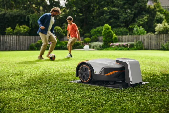 STIHL iMOW 6 Mähroboter mit Dockingstation im Garten, spielende Personen