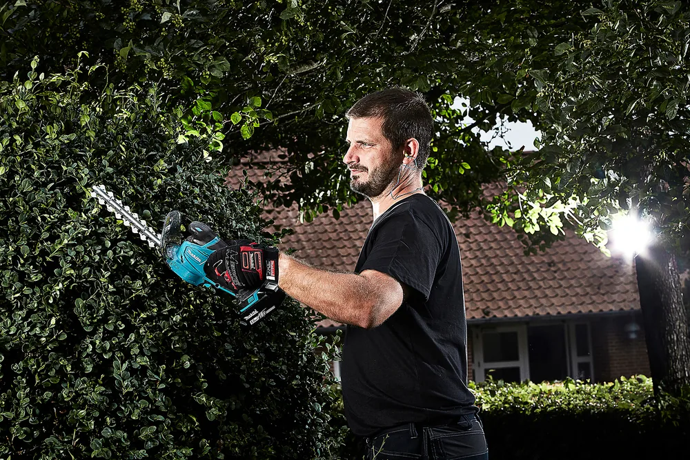 Mann schneidet eine Hecke mit dem Strauchmesser der Makita DUM604ZX
