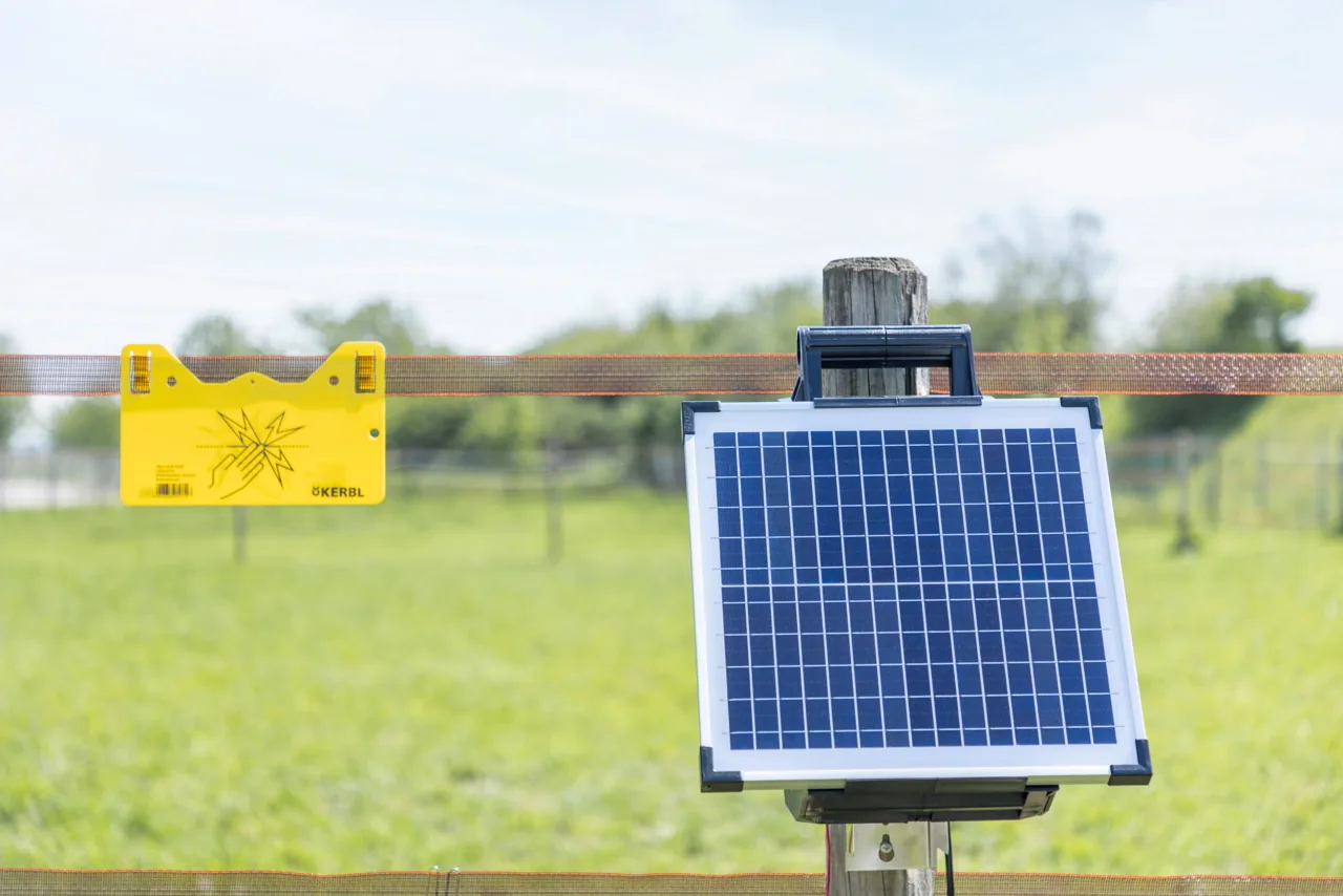 Kerbl Sun Power S 1500 Solarmodul auf Zaunpfosten neben gelbem Warnschild auf grüner Weide
