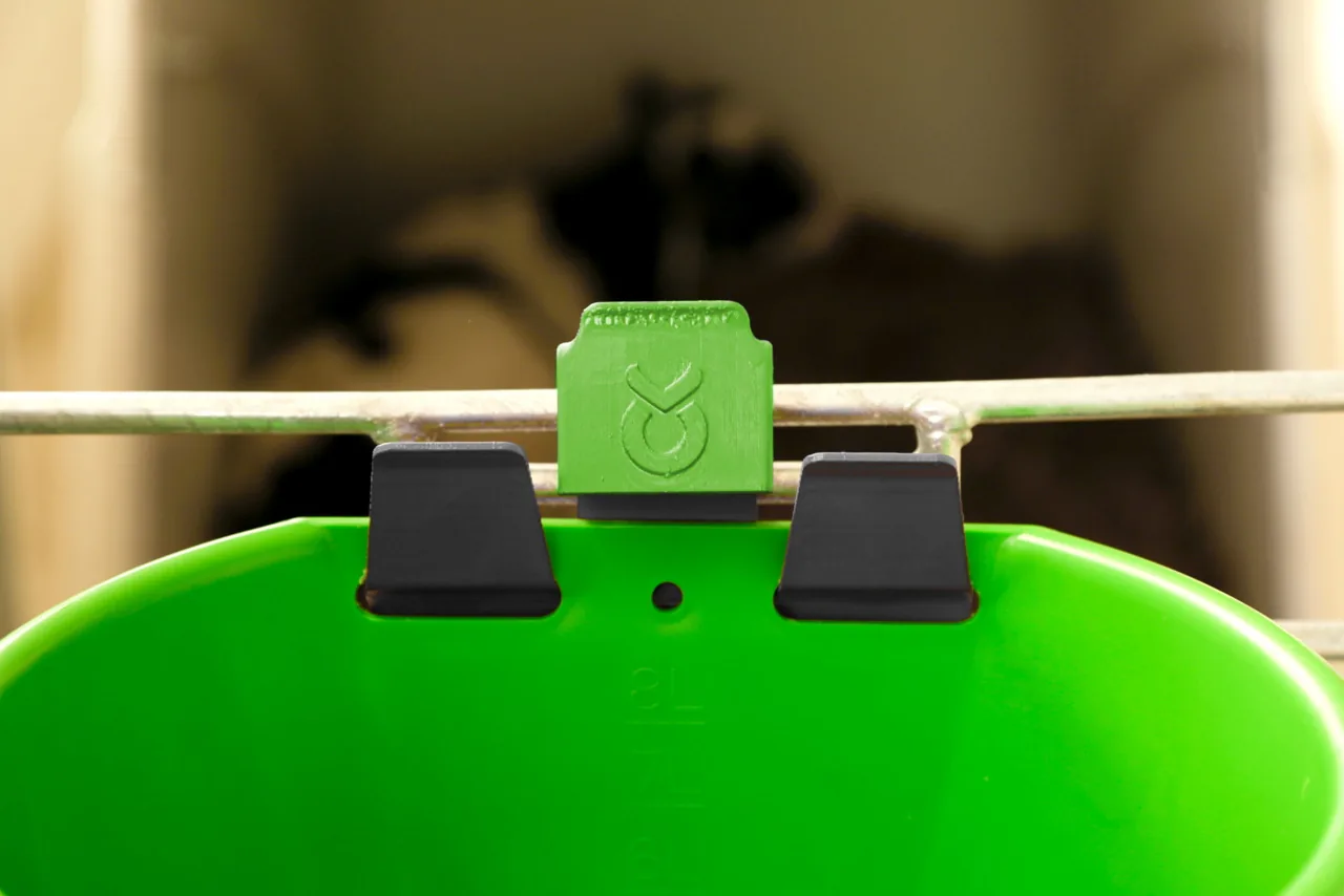 Detailaufnahme des grünen Bucket-Guard-Halters auf einem Eimer im Stall