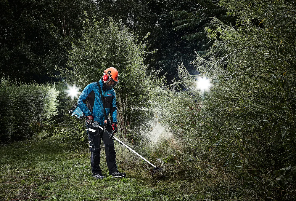 Mann mäht mit dem Makita DUX60Z und Freischneider-Aufsatz dichten Bewuchs