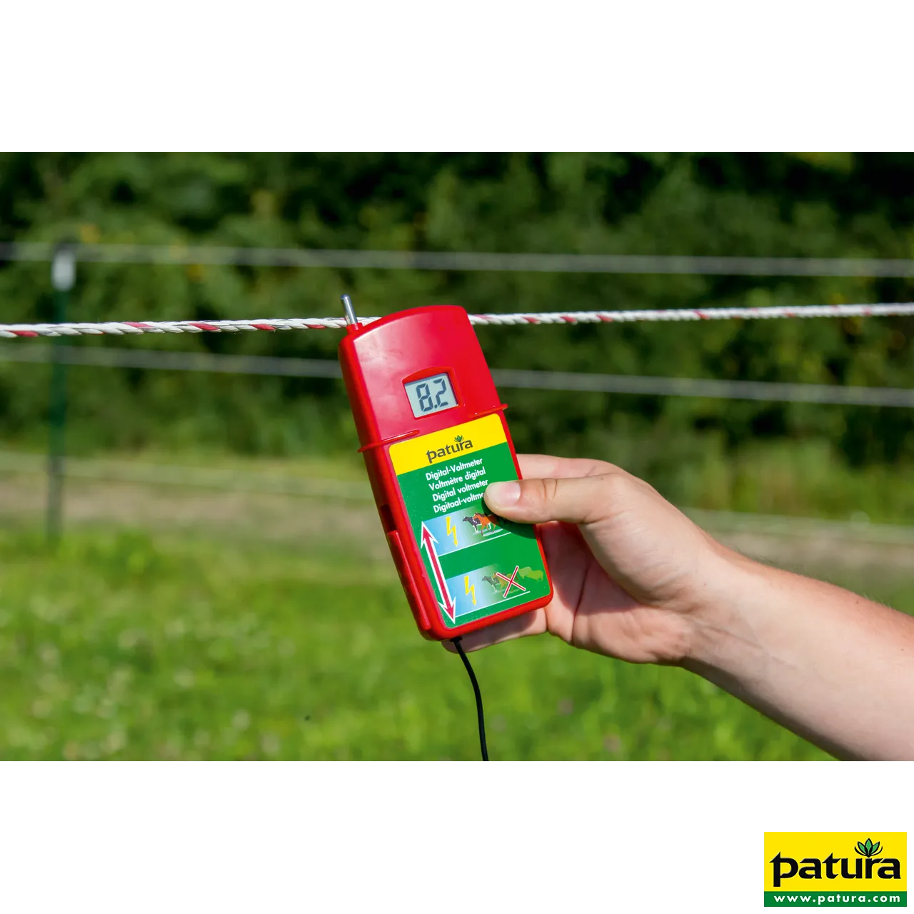 Hand hält das rote Patura Digital-Voltmeter mit Display am Elektrozaun