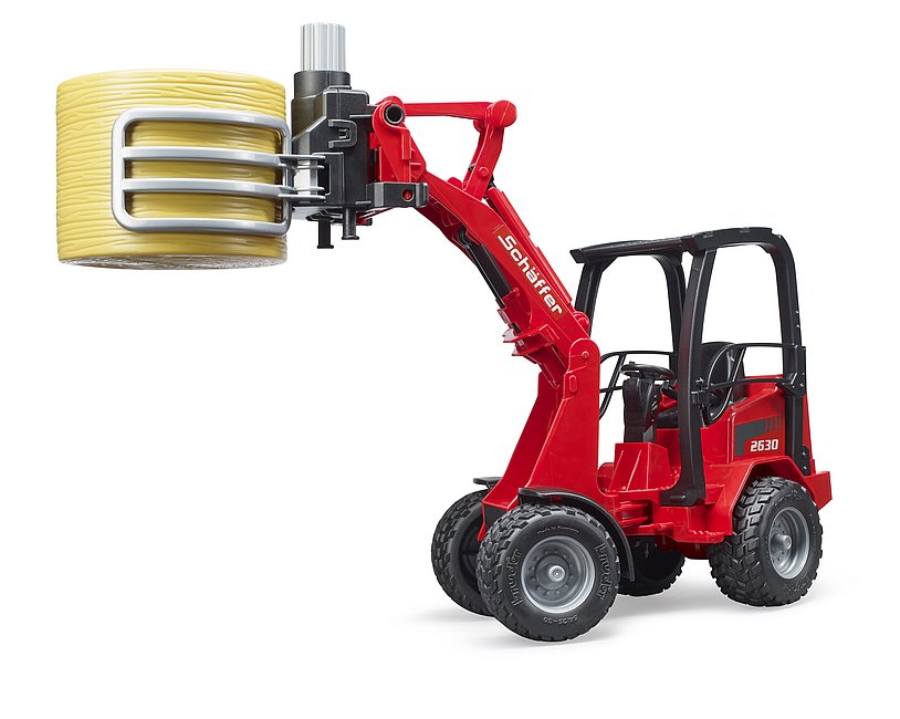 Schäffer Hoflader hebt einen gelben Rundballen mit der Ballenzange an