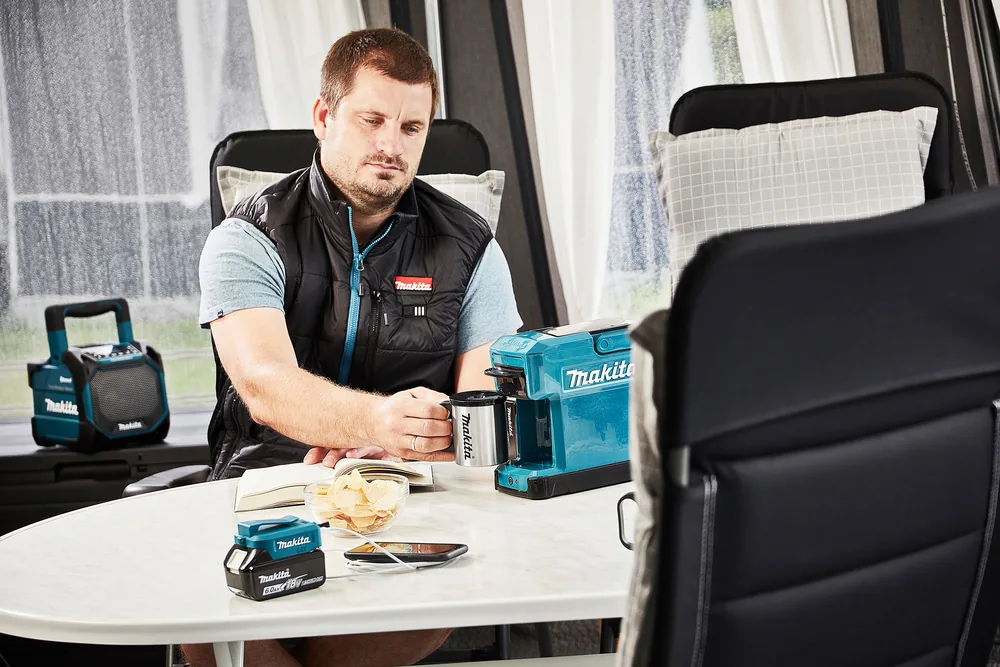 Mann bereitet mit der Makita DCM501Z Akku-Kaffeemaschine unterwegs Kaffee zu