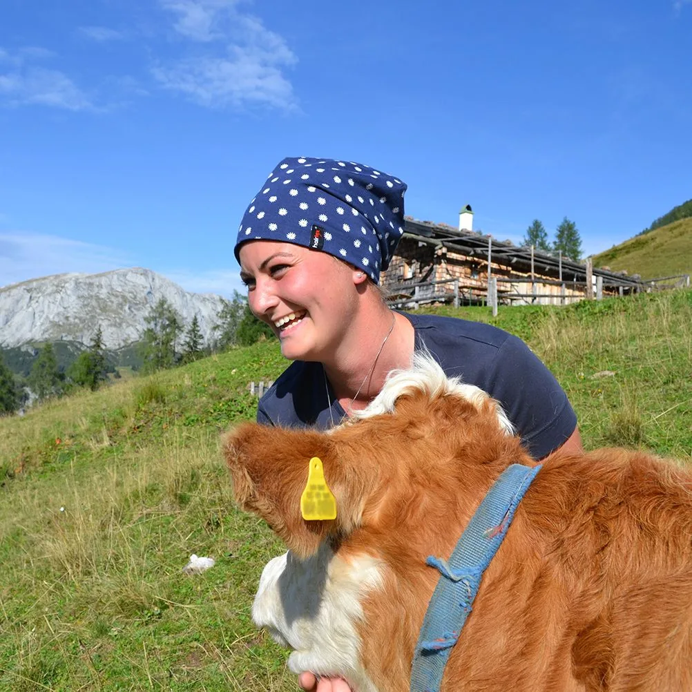 Lächelnde Frau mit Hairtex Stall-Beanie und einem Kalb auf der Alm