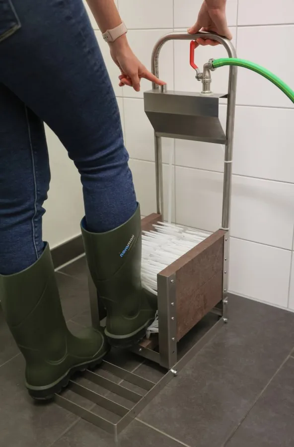 Person reinigt Gummistiefel am Edelstahl-Stiefelreiniger mit Wasserschlauch