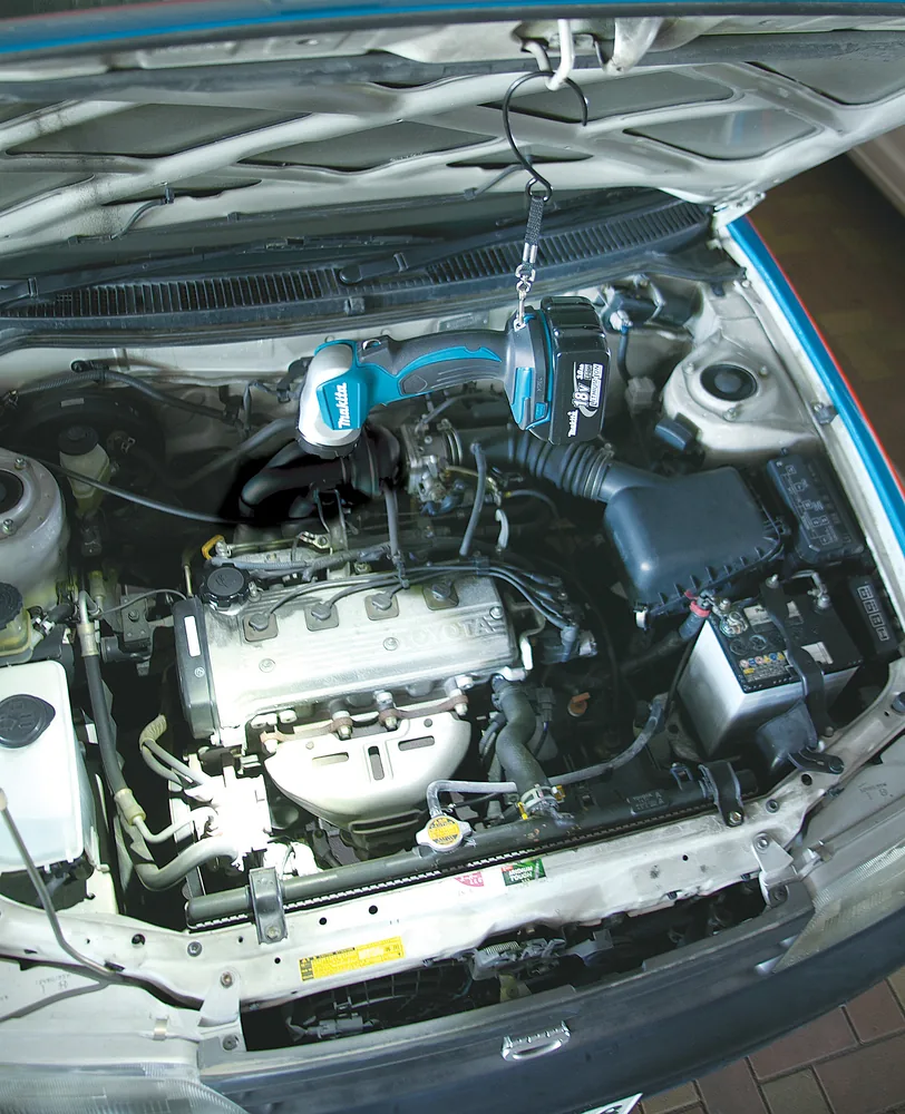 Makita DEBDML802 Akku-LED-Handleuchte aufgehängt im Motorraum eines Fahrzeugs