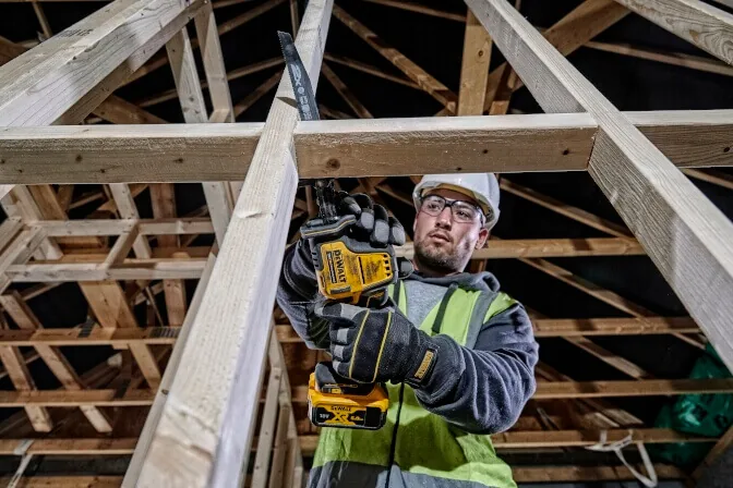 Mann mit DeWalt DCS369NT Akku-Säbelsäge über Kopf im Dachstuhl