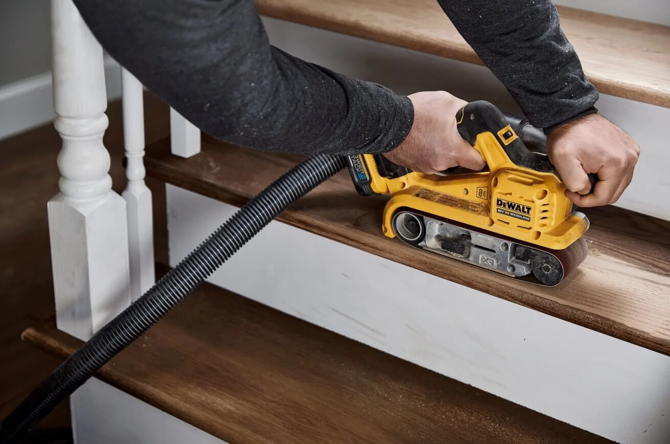 DeWalt DCW220NT Akku-Bandschleifer im Einsatz an einer Treppe mit Absaugschlauch