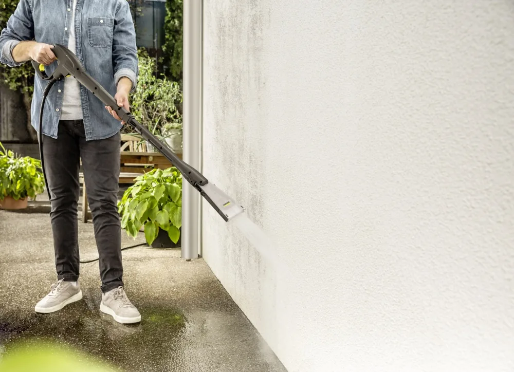 Person reinigt eine Hauswand mit dem Kärcher eco!Booster Strahlrohr