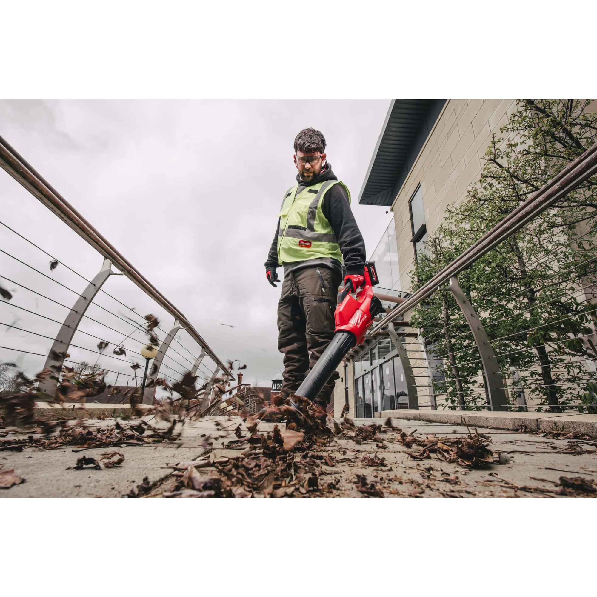 Mann bläst mit dem Milwaukee M18 FBL-0 Laub auf einem Gelände