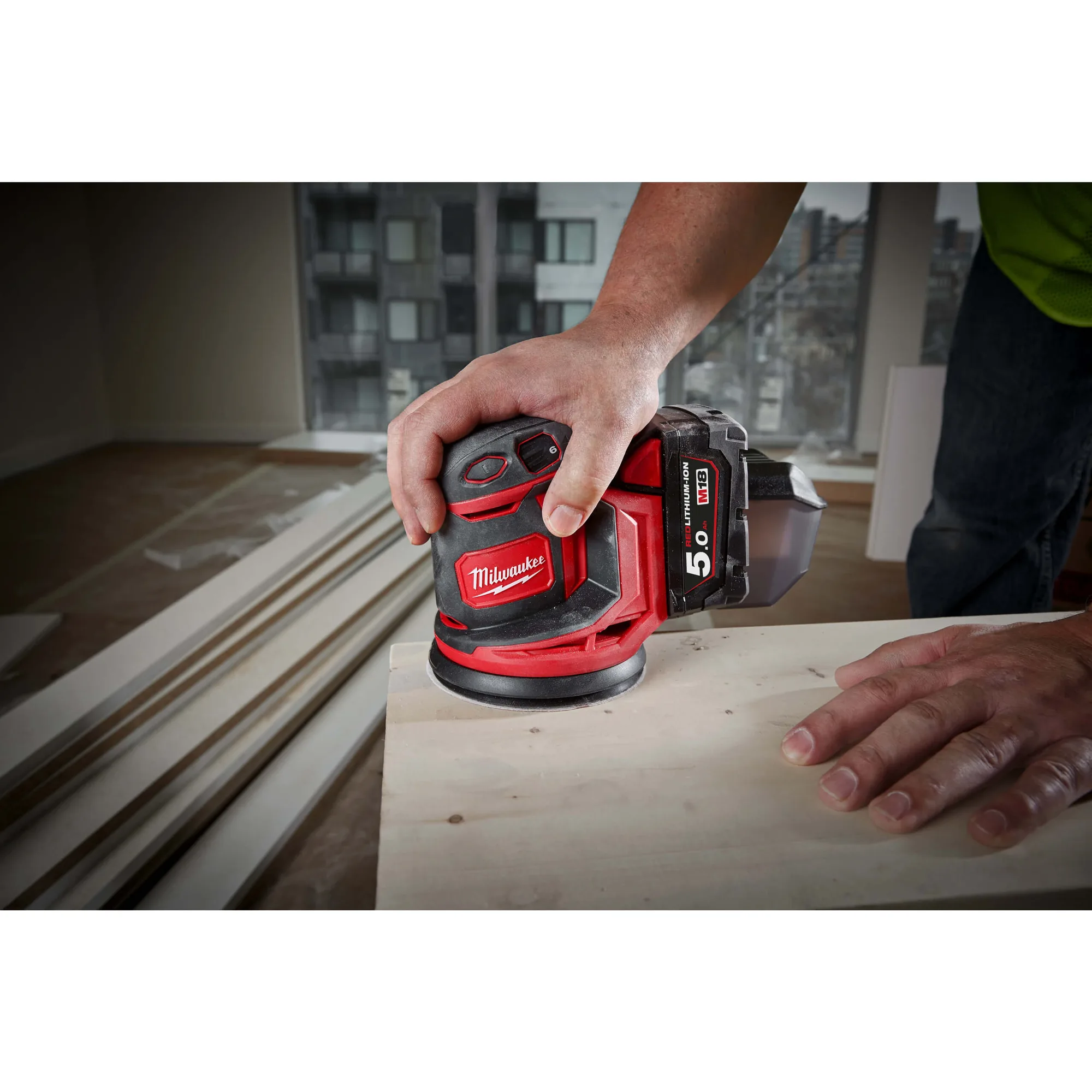 Milwaukee M18 BOS125 Exzenterschleifer beim Schleifen einer Holzplatte