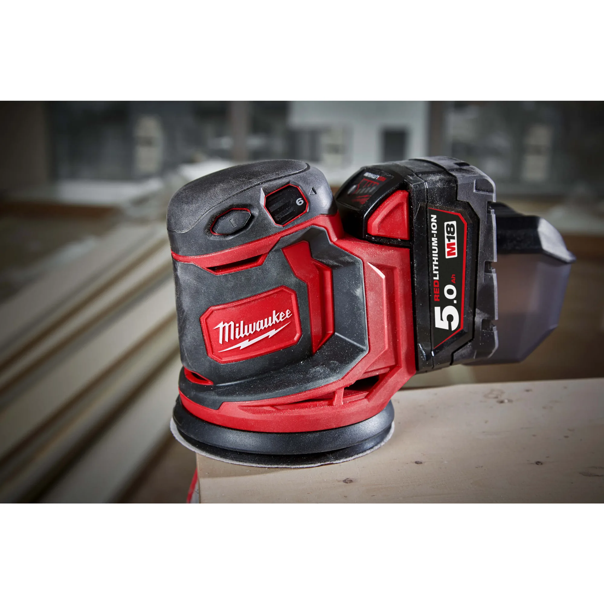 Milwaukee M18 BOS125 Exzenterschleifer mit Akku auf einem Holzbrett