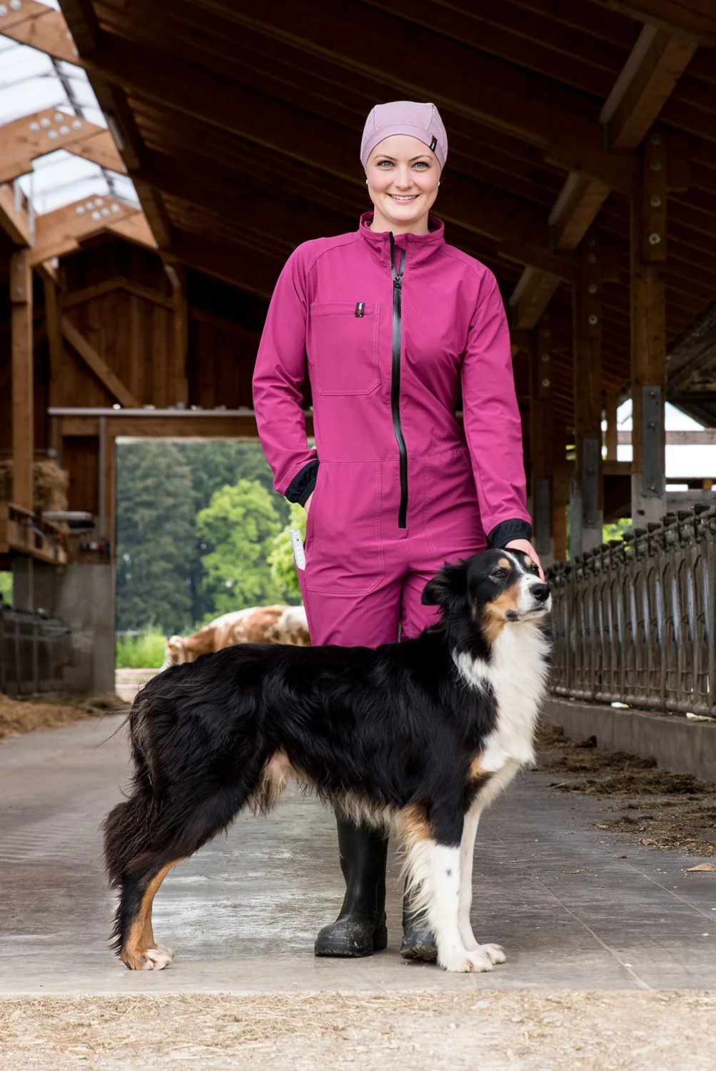 Frau im pinken Hairtex Damen-Overall im Stall mit Hütehund