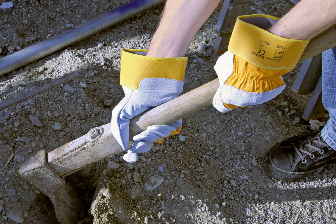 Behandschuhte Hände greifen einen Holzbalken auf der Baustelle