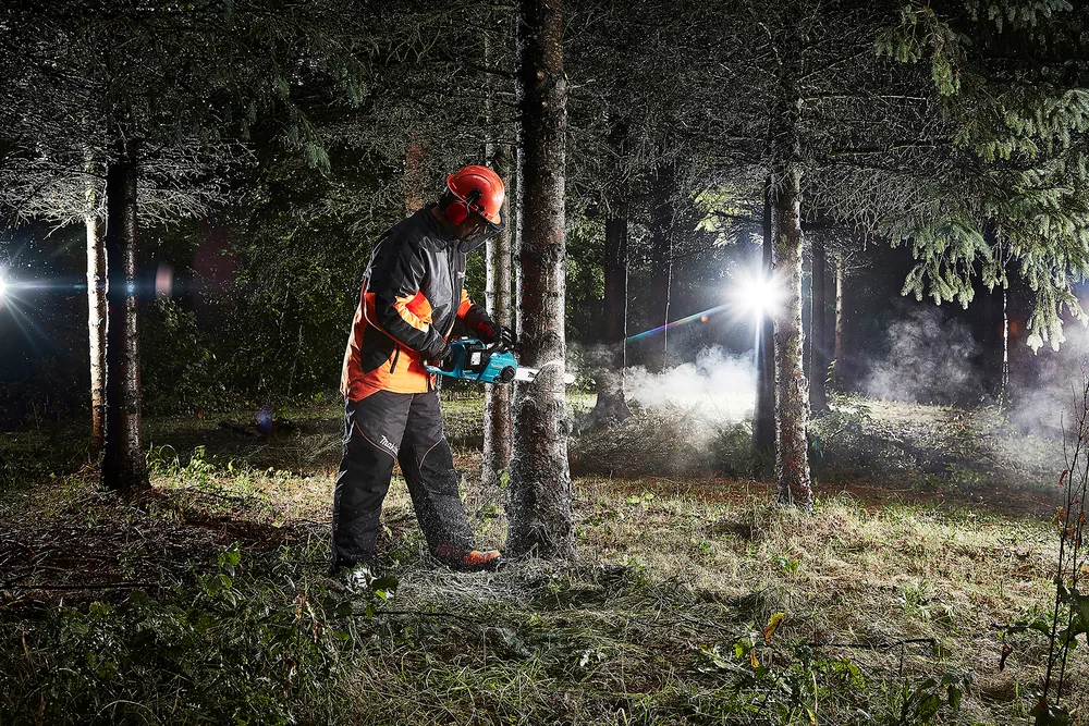 Mann fällt einen Baum mit der Makita DUC353Z Kettensäge bei wenig Licht im Wald