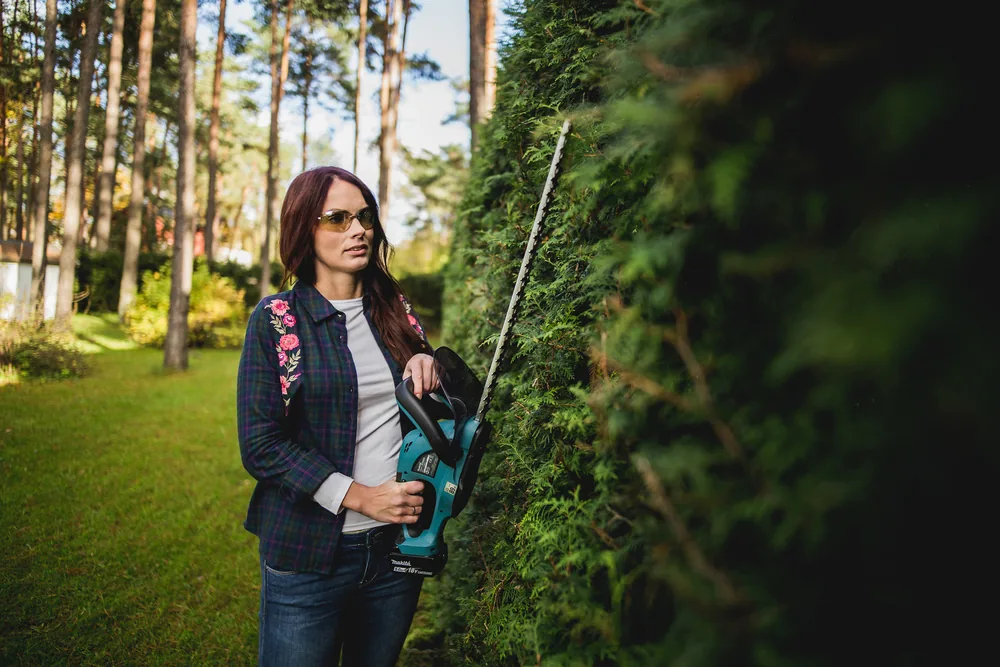 Frau mit der Makita DUH523Z Akku-Heckenschere an einer hohen Hecke