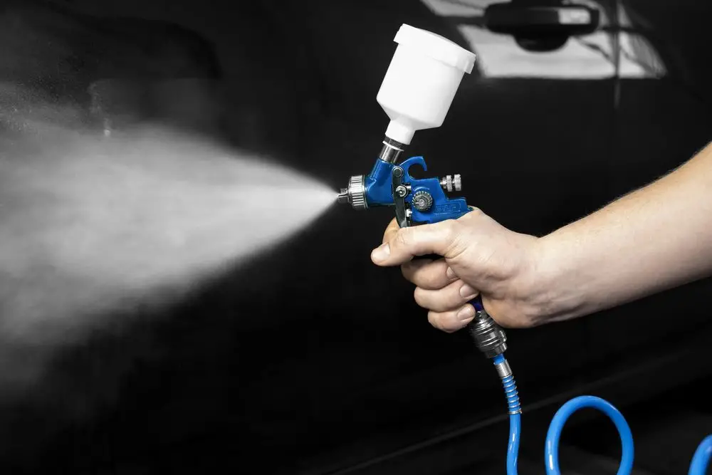 Güde Farbspritzpistole PROFI-M sprüht blaue Farbe, in der Hand vor dunklem Hintergrund