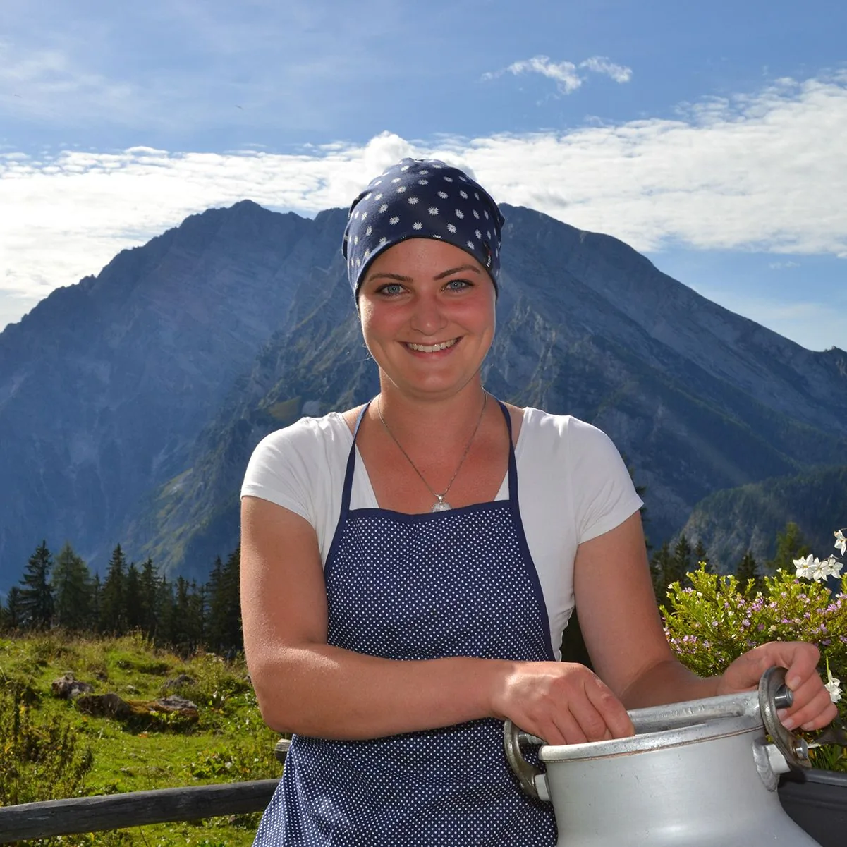 Frau mit Hairtex Stall-Beanie vor Bergpanorama, mit Milchkanne