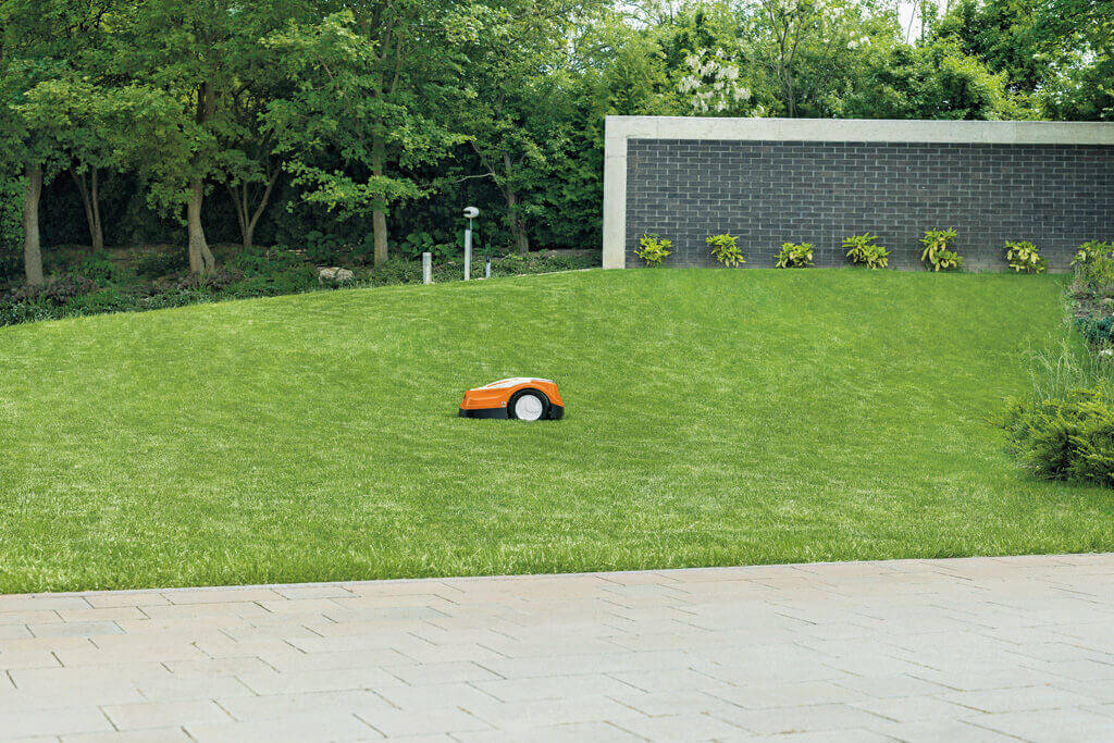 STIHL RMI 422 P Mähroboter auf gepflegtem Rasen vor einer Gartenmauer
