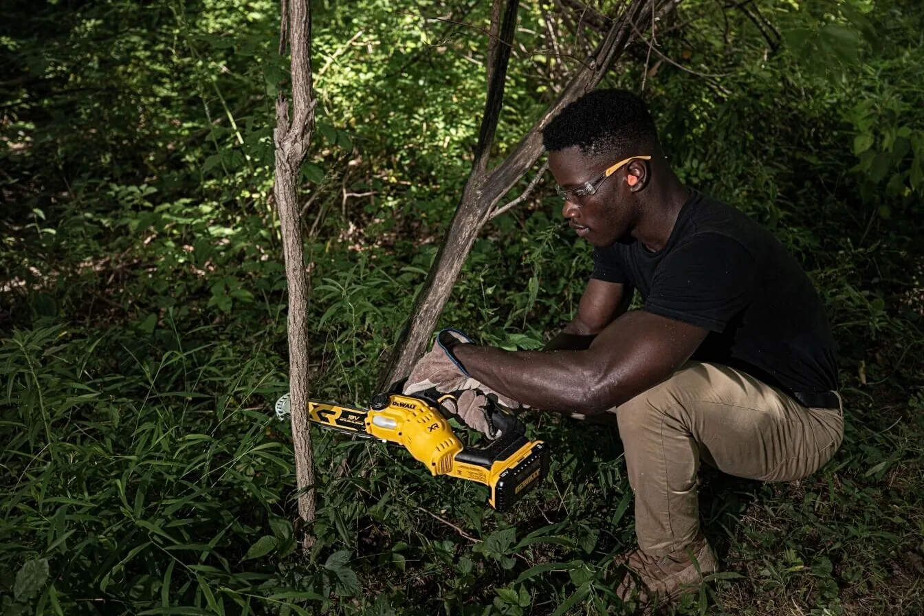 Anwender entastet mit der DeWalt DCMPS520N einen Baumstamm bodennah