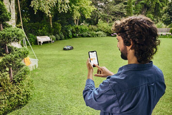 Mann steuert den STIHL iMOW 6 EVO Mähroboter per Smartphone-App im Garten