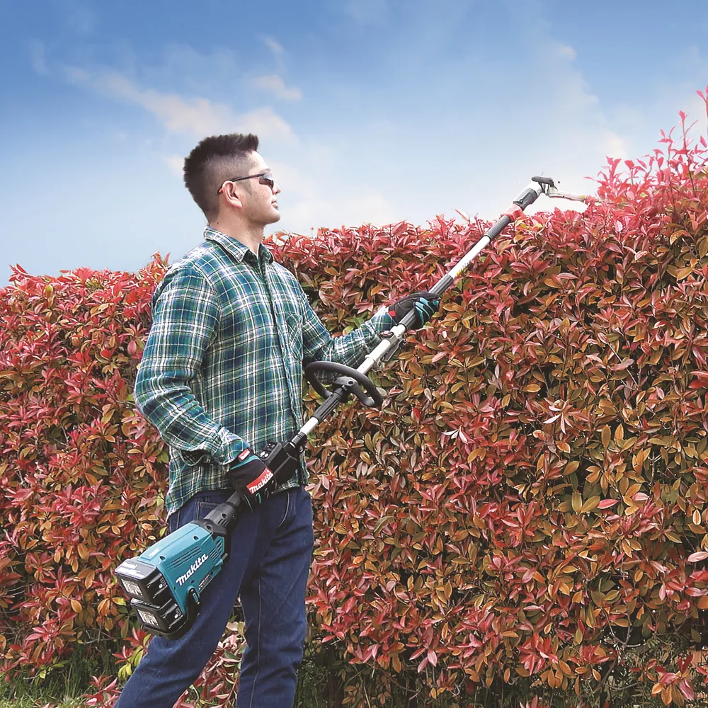 Mann schneidet mit dem Makita DUX60Z und Heckenschneider-Aufsatz eine rote Hecke