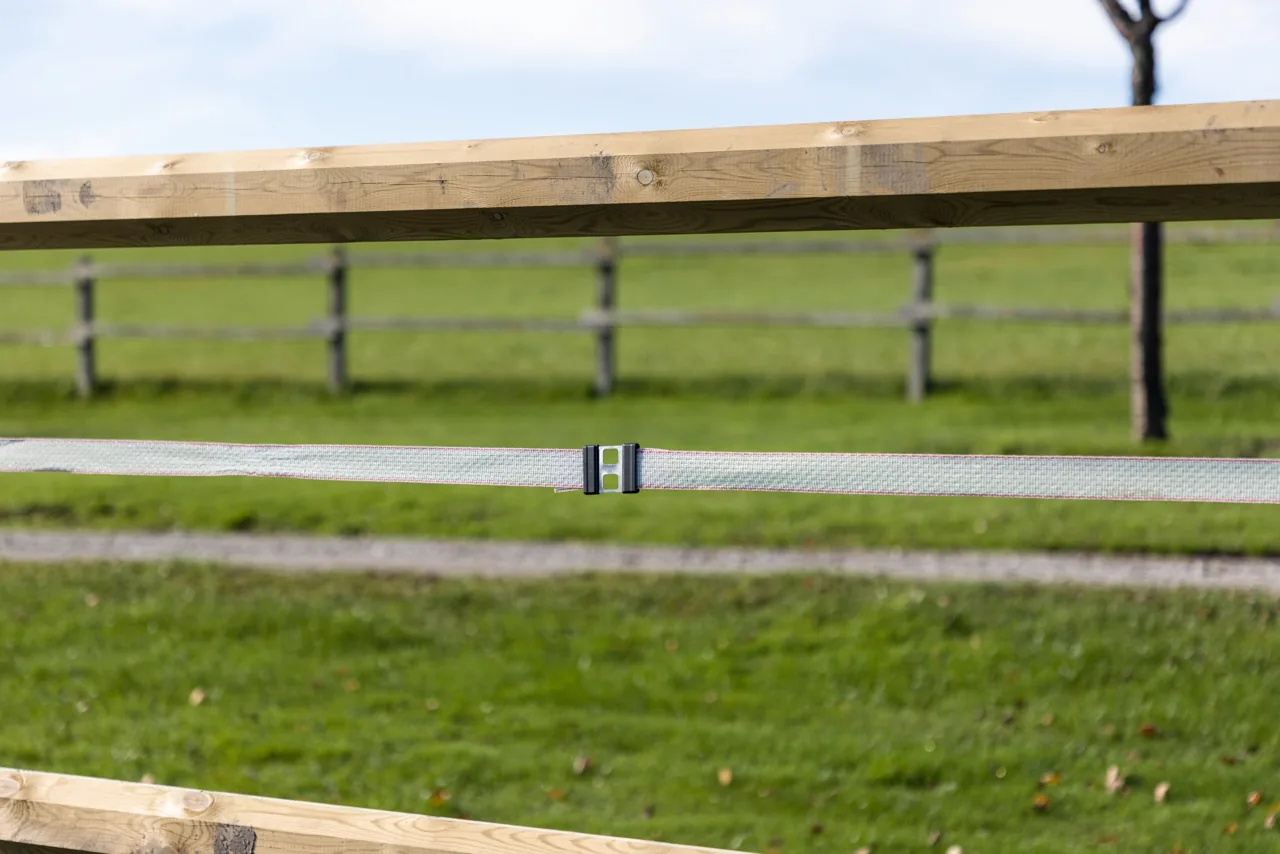 Weidezaun mit weißem Band und Litzclip-Bandverbinder, Holzkoppel im Hintergrund
