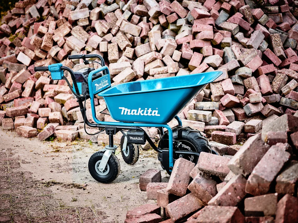 Blaue Makita DCU180Z Akku-Schubkarre vor einem Ziegelhaufen