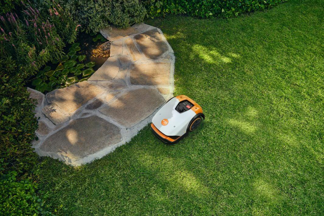STIHL iMOW 4 Mähroboter auf dem Rasen neben einem Steinweg
