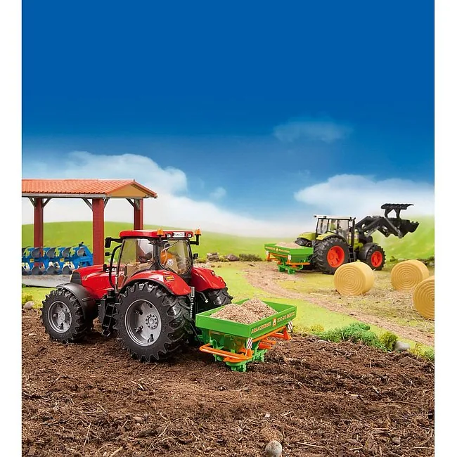 Roter Spielzeug-Traktor mit grünem BRUDER Amazone Zentrifugalstreuer auf dem Feld