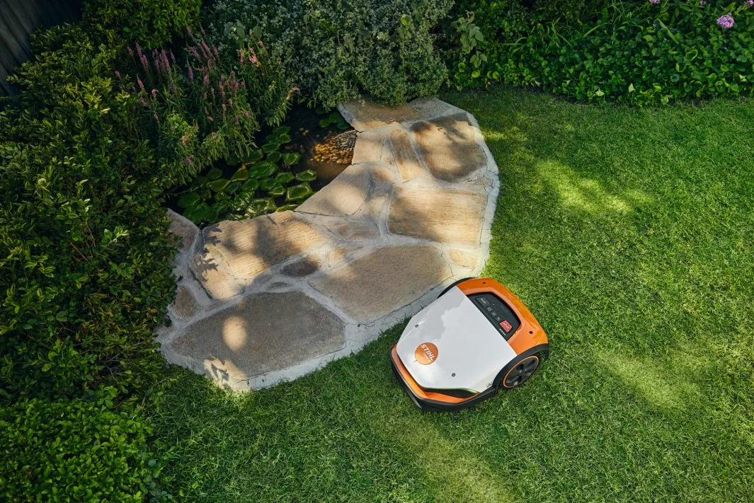 STIHL iMOW 7 Mähroboter aus der Vogelperspektive auf Rasenfläche neben Gartenweg